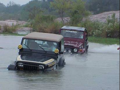 [Two jeeps crossing the river heading into deeper water]